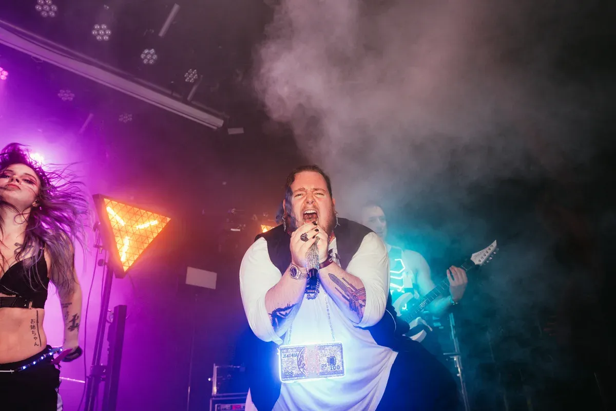 Saenger schreit ins Mikrofon zwischen Taenzerin und Gitarrist im Nebel