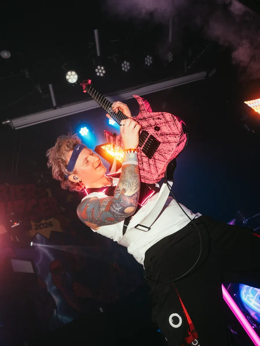 Bassist spielt pinke Gitarre ueber dem Kopf im Rauch